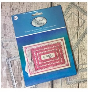 May include: A package of six metal die cuts for crafting. The die cuts are in the shape of nested rectangles with a decorative border. The package is blue and white with the words "Craft Buddy" and "Decorative Nested Rectangles" printed on it. The die cuts are shown on a pink background with the words "With Love" written inside the smallest rectangle.