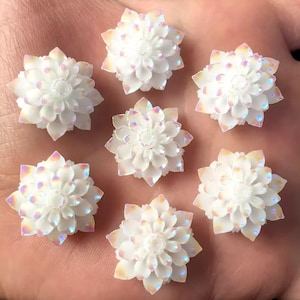 Op de afbeelding: Zeven witte, iriserende, bloemvormige versieringen met een verhoogd midden. De versieringen zijn ongeveer 2,5 cm in diameter.