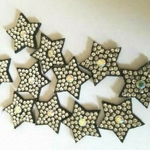 May include: A collection of 11 black star-shaped embellishments with rhinestones. Each star has a black outline and is covered in clear rhinestones.