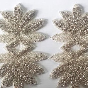 May include: Two silver rhinestone embellishments in the shape of a flower with multiple layers of petals.