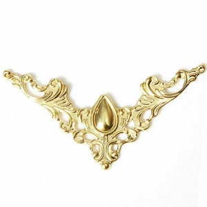 May include: Gold metal decorative trim with a teardrop-shaped center piece. The trim has a delicate, ornate design with a scalloped edge.