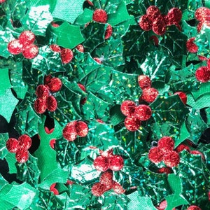 May include: A close-up of a pile of green and red glitter holly leaves and berries. The leaves are shiny and have a metallic finish. The berries are red and have a textured surface.