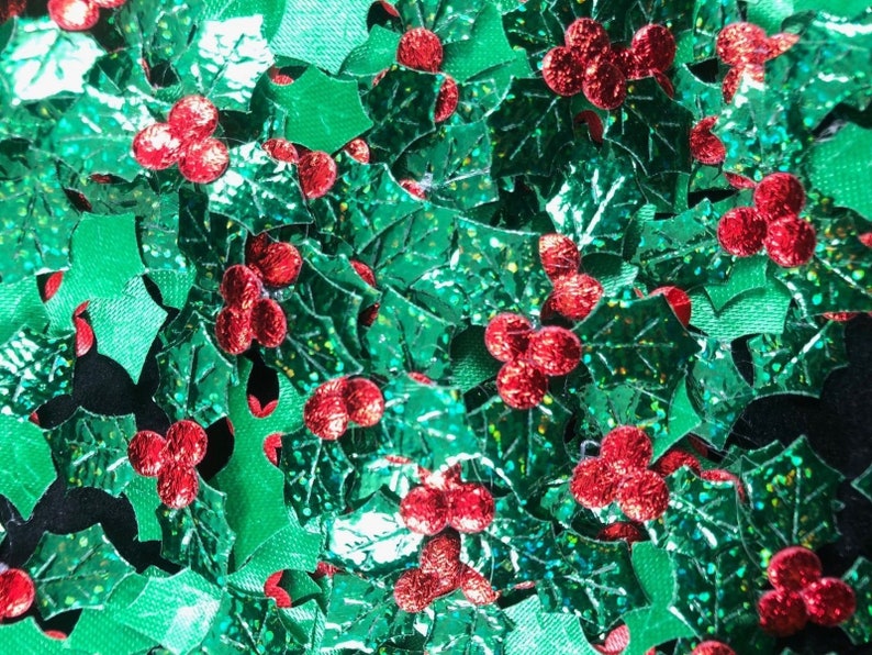May include: A close-up of a pile of green and red glitter holly leaves and berries. The leaves are shiny and have a metallic finish. The berries are red and have a textured surface.