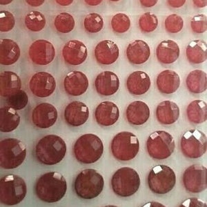 May include: A sheet of 40 small, round, red, faceted rhinestones. The rhinestones are arranged in a grid pattern.