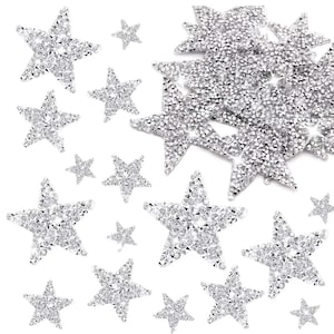 May include: A collection of sparkling, silver star-shaped embellishments. The stars vary in size and are covered in reflective, glittering rhinestones. These decorative elements are ideal for crafts, scrapbooking, or adding a touch of glamour to various projects.
