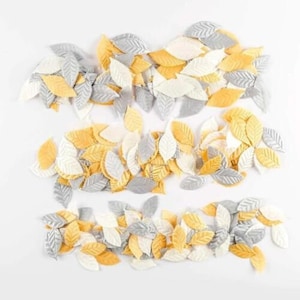 May include: A collection of yellow, white, and gray felt leaves. The leaves are scattered on a white background.
