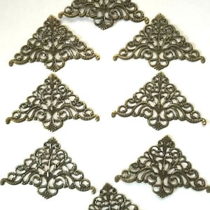 May include: Eight antique gold-toned metal corner embellishments with a filigree design. Each corner piece is triangular in shape.