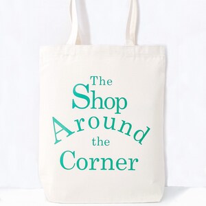 May include: A white canvas tote bag with teal blue text that reads "The Shop Around the Corner".
