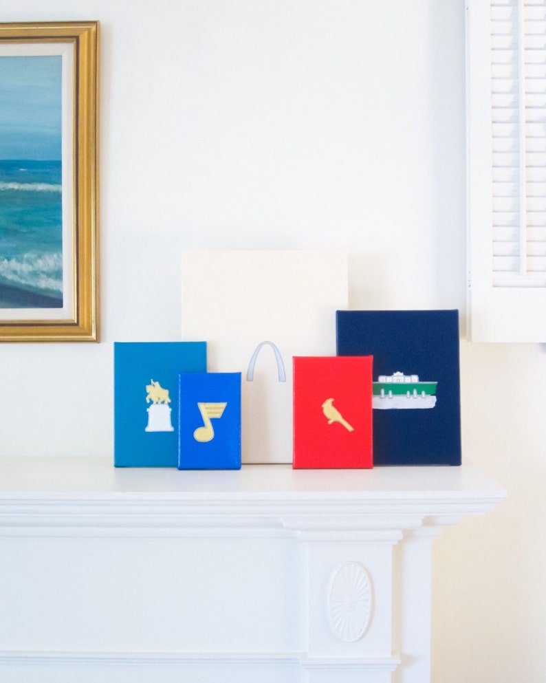 May include: Five framed prints with different designs, including a musical note, a cardinal, a bull, a gateway arch, and a boat. The prints are arranged on a white mantelpiece.