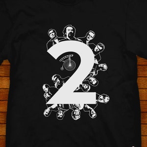 Könnte beinhalten: Schwarzes T-Shirt mit einer weißen Zahl "2" in der Mitte. Die Zahl ist von einem Kreis aus weißen Silhouetten von Personen umgeben.