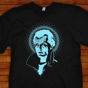 May include: Black t-shirt with a blue graphic of a man's face with a circuit board design in his forehead. The graphic is surrounded by a blue geometric pattern. The text "JARED SWART artwork + apparel" is at the bottom of the shirt.