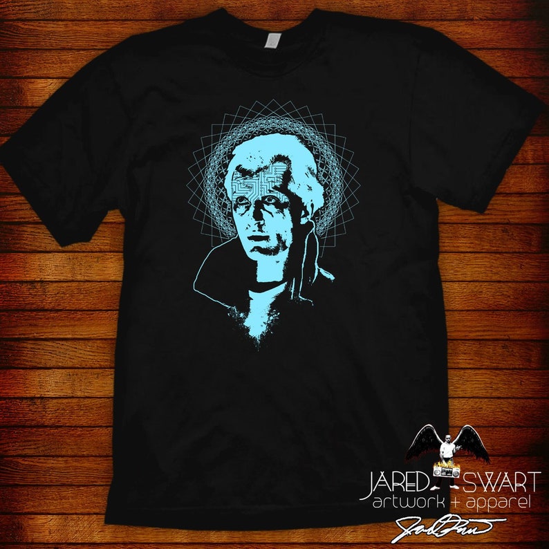 May include: Black t-shirt with a blue graphic of a man's face with a circuit board design in his forehead. The graphic is surrounded by a blue geometric pattern. The text "JARED SWART artwork + apparel" is at the bottom of the shirt.
