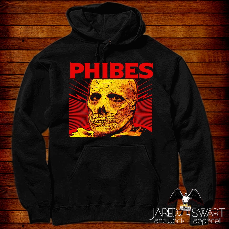 Pode incluir: Camisola de capuz preta com uma estampa gr&aacute;fica vermelha e amarela de um rosto de caveira com o texto "PHIBES" acima.