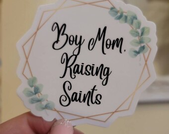 May include: White sticker with a gold geometric frame and green foliage. The text reads "Boy Mom. Raising Saints."