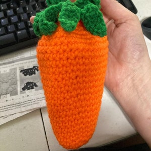 May include: A crocheted carrot toy with green leaves. The carrot is orange and the leaves are green.
