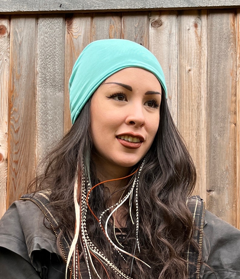 May include: A woman with long, dark hair wearing a light blue beanie. She has feather hair extensions in her hair.