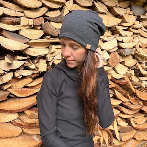 May include: A charcoal gray beanie with a brown logo. The beanie is made of a soft, stretchy fabric and has a slouchy fit.