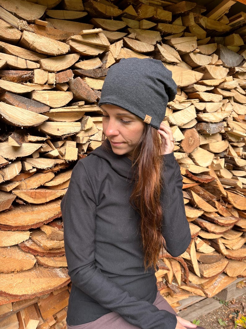 May include: A charcoal gray beanie with a brown logo. The beanie is made of a soft, stretchy fabric and has a slouchy fit.