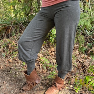 Op de afbeelding: Grijze wijde broek met een losse pasvorm en een lichte flare aan de onderkant. De broek wordt gedragen met bruine leren enkellaarsjes met franjes.