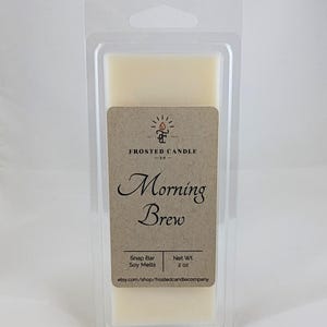 Op de afbeelding: Een kleine, doorzichtige plastic container bevat een witte sojawas smelt. Het etiket is bruin met witte tekst die "FROSTED CANDLE -63- Morning Brew Snap Bar Soy Melts Net Wt. 2 OZ etsy.com/shop/frostedcandlecompany" luidt.