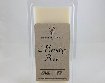 May include: A small, clear plastic container holds a white soy wax melt. The label is brown with white text that reads "FROSTED CANDLE -63- Morning Brew Snap Bar Soy Melts Net Wt. 2 OZ etsy.com/shop/frostedcandlecompany"