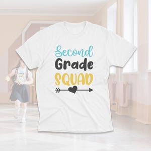 May include: White t-shirt with the text "Second Grade Squad" in blue and yellow lettering with a black arrow and heart.