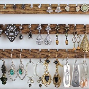 May include: A wooden earring holder with three rows of earrings. The earrings are a variety of styles, including silver, gold, and turquoise. Some earrings feature crystals, others have beads, and some have a more rustic look.