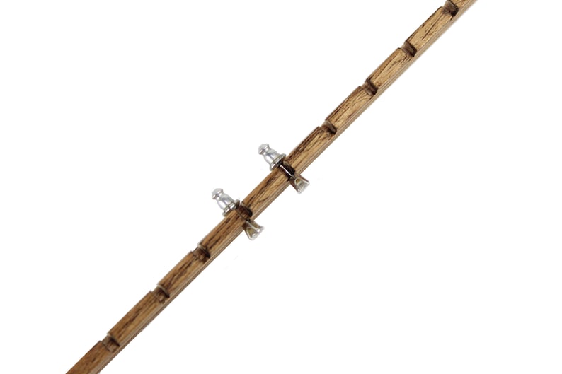 May include: A long, narrow, brown wooden strip featuring a series of evenly spaced notches along its length. Two small, silver-colored metal earring backs are attached to the wooden strip, positioned within two of the carved notches.