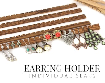 May include: A set of dark brown wooden earring holder slats with notched edges for hanging jewelry. The display features various earrings including crystal drops, turquoise, pearl, rose-shaped, and green teardrop designs. Text reads EARRING HOLDER INDIVIDUAL SLATS.