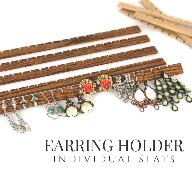 May include: A set of dark brown wooden earring holder slats with notched edges for hanging jewelry. The display features various earrings including crystal drops, turquoise, pearl, rose-shaped, and green teardrop designs. Text reads EARRING HOLDER INDIVIDUAL SLATS.