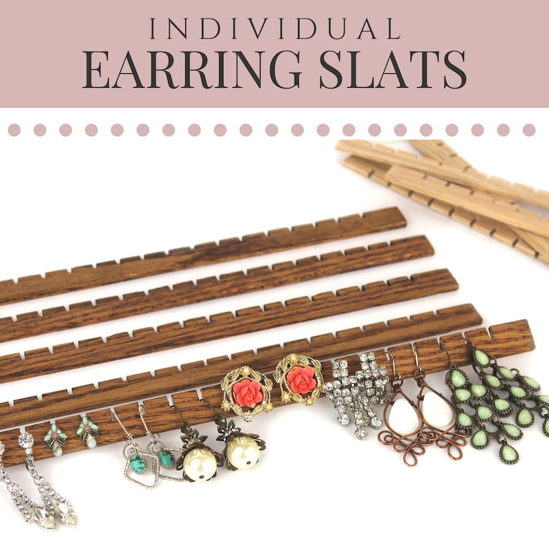 May include: Dark brown wooden earring slats with evenly spaced notches for jewelry organization. The text INDIVIDUAL EARRING SLATS is printed at the top. Several pairs of earrings, including crystal, pearl, and green stone designs, hang from the slats.