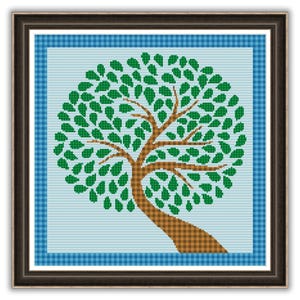 May include: A framed cross-stitch of a tree with a brown trunk and branches, and a full crown of green leaves. The tree is set against a light blue background with a blue plaid border. The frame is dark brown.