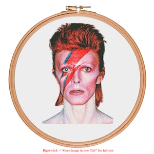May include: A cross-stitch embroidery of David Bowie with red, blue, and black makeup on his face. The background is white.