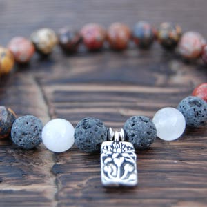 May include: A beaded bracelet featuring a variety of natural stone beads in shades of red, brown, gray, and white. The bracelet includes a silver-colored rectangular charm with a floral design. The beads are approximately 0.4 inches in diameter.
