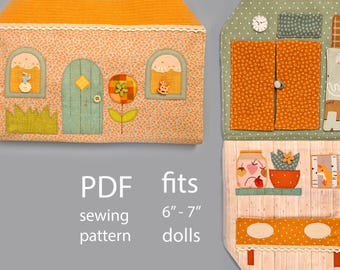 May include: A fabric dollhouse sewing pattern with an orange roof and a light peach-colored body. The dollhouse has a green door, windows, and a flower applique. The interior features a bed, cabinets, and a shelf with jars and a fox illustration. Fits 6" - 7" dolls.