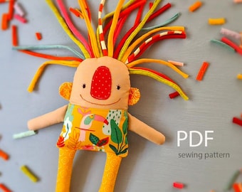 May include: A fabric doll with a quirky design. The doll has a tan face, a red nose, and colourful yarn hair. It wears a yellow shirt with a tropical pattern and yellow patterned legs. The text "PDF sewing pattern" is visible.