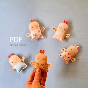 Puede incluir: Cinco muñecos de tela hechos a mano con los ojos cerrados, brazos pequeños y pelo naranja. Los muñecos tienen diferentes patrones de tela en el vientre, incluyendo diseños florales, de lunares y de corazones. El texto "PDF sewing pattern" es visible.