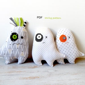 May include: Three handmade monster plushies. The first is gray and white patterned with a green button eye and black button. The second is white with gold dots and a black and white button eye. The third is white with black dots and an orange button eye. Text: PDF sewing pattern.