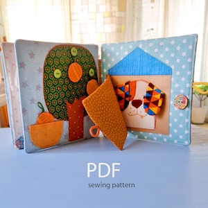 May include: A handmade fabric quiet book with colorful appliqued designs. One page features a tree with orange fruit and green buttons, the other a dog in a house. The book is light blue with white polka dots and stars. The text "PDF sewing pattern" is at the bottom.