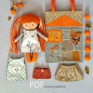 Puede incluir: Una muñeca hecha a mano con cabello naranja y un vestido blanco con un estampado de árbol. La muñeca está junto a un bolso a juego y ropa de muñeca adicional. El bolso tiene un diseño de casa con detalles en naranja y gris. El texto "PDF sewing pattern" es visible.