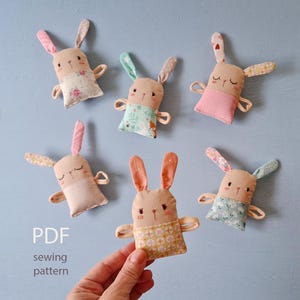 以下が含まれることがあります： 様々な柄の生地のアクセントが付いた、手作りのウサギのぬいぐるみ6体。ウサギは、ベージュの体、ピンクまたは青の耳、刺繍された顔の特徴を持っています。「PDF sewing pattern」というテキストが左下に表示されています。