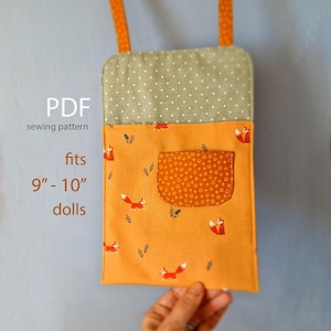 Puede incluir: Bolso de muñeca naranja con estampado de zorros y un pequeño bolsillo, diseñado para muñecas de 23-25 cm. La parte superior es verde con lunares blancos. El bolso tiene correas naranjas y el texto "PDF sewing pattern" es visible.