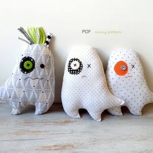 May include: Three handmade fabric monster dolls with button eyes and stitched mouths. The dolls have different patterned fabrics, including geometric and polka dot designs. One doll has green and black hair. The text "PDF sewing pattern" is visible.
