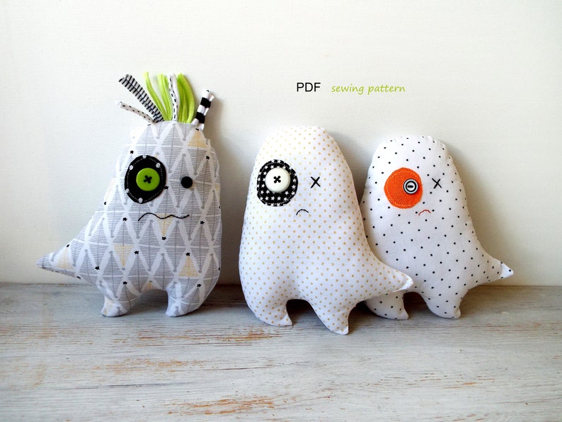 May include: Three handmade fabric monster dolls with button eyes and stitched mouths. The dolls have different patterned fabrics, including geometric and polka dot designs. One doll has green and black hair. The text "PDF sewing pattern" is visible.