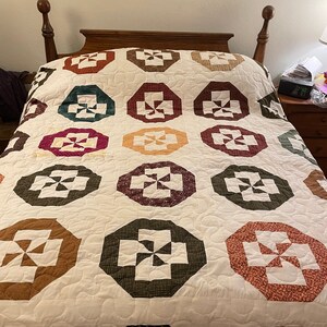 May include: A white quilt with a patchwork design featuring a repeating pattern of octagons with a pinwheel design in various colors, including brown, green, red, and white.
