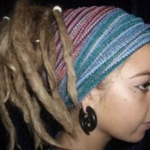 May include: A person with long blonde dreadlocks is wearing a blue and pink striped headband. The headband is tied at the back of the head. The person has a black hoop earring in their left ear.