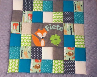 Peut inclure: Une courtepointe en patchwork avec un renard, un trèfle et le nom "Fiete" brodé dessus. La courtepointe est faite de différents tissus dans des tons de vert, bleu, gris et blanc.