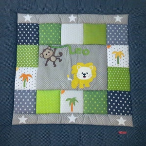 Peut inclure: Une couverture bébé en patchwork multicolore avec un lion, un singe et des palmiers. La couverture est personnalisée avec le nom "Leo" brodé dessus.
