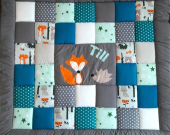 Peut inclure: Une courtepointe bébé en patchwork avec une bordure grise et une variété de carrés colorés. La courtepointe représente un renard, un loup et un ours, ainsi que des étoiles, des arbres et d'autres motifs de forêt. La courtepointe est personnalisée avec le nom "Till".