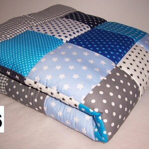 Peut inclure: Une courtepointe en patchwork avec une variété de tissus bleus, gris et blancs. La courtepointe est composée de carrés avec différents motifs, notamment des pois, des étoiles et du vichy. La courtepointe est pliée en deux et le numéro 66 est visible dans le coin inférieur gauche.